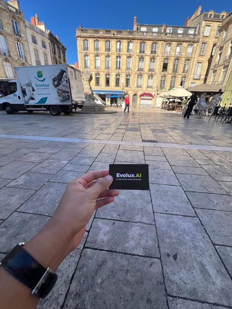 Une main tient une carte de visite Evolux sur une place de Bordeaux