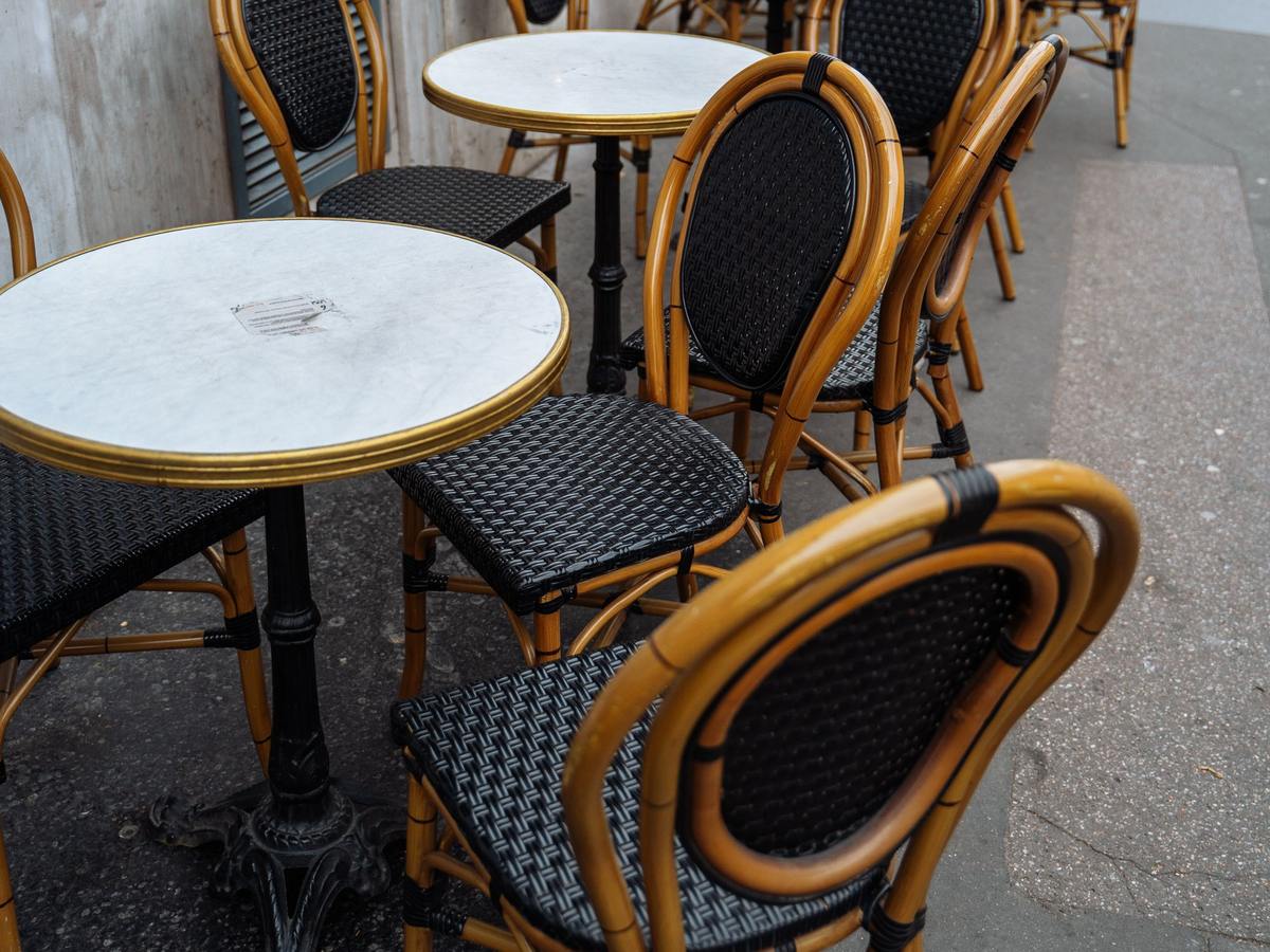Terrasse de café avec des tables rondes à plateau de marbre et des chaises en rotin tressé