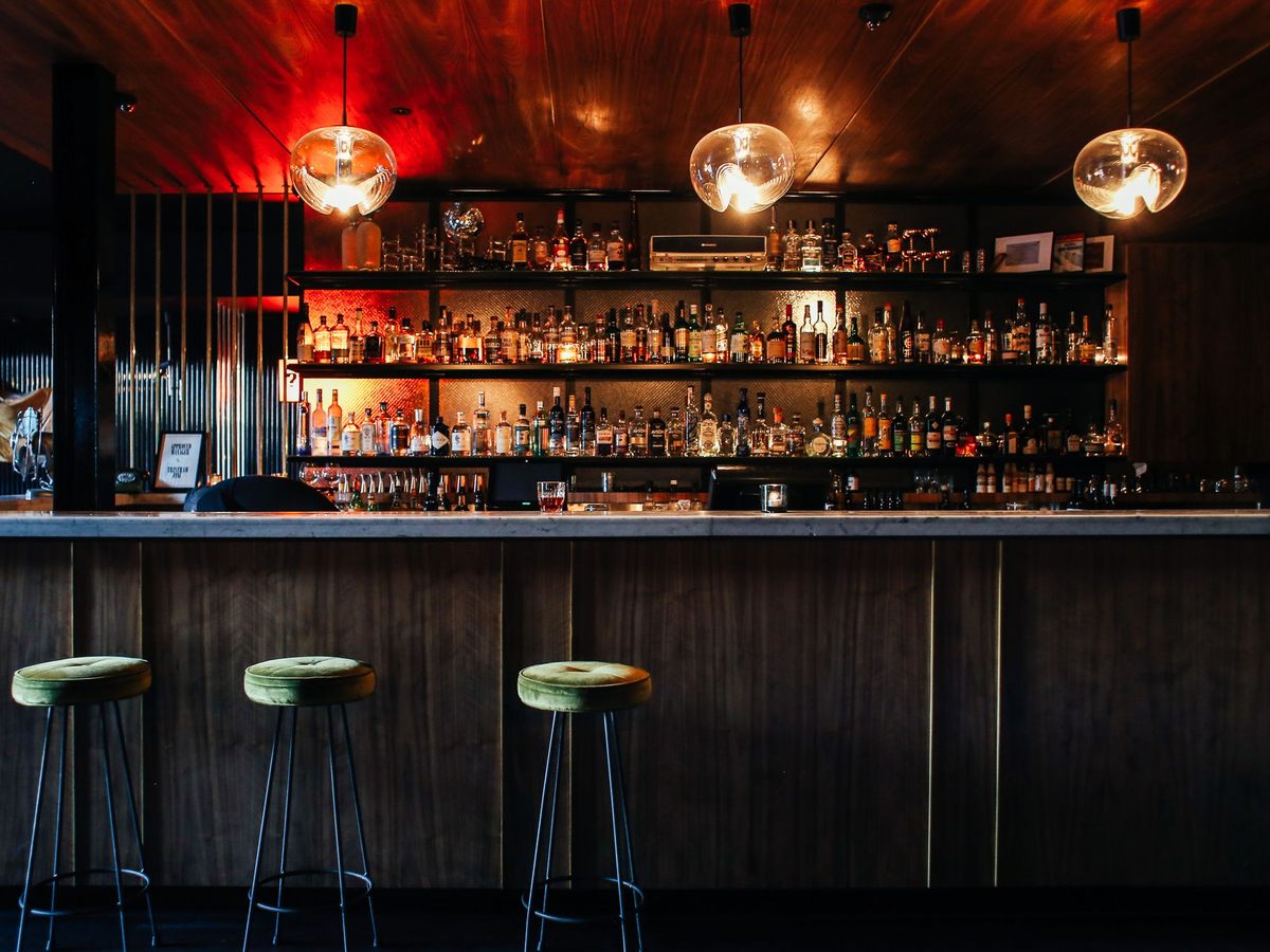 Comptoir de bar en bois avec des tabourets verts et des étagères de bouteilles éclairées sous des suspensions