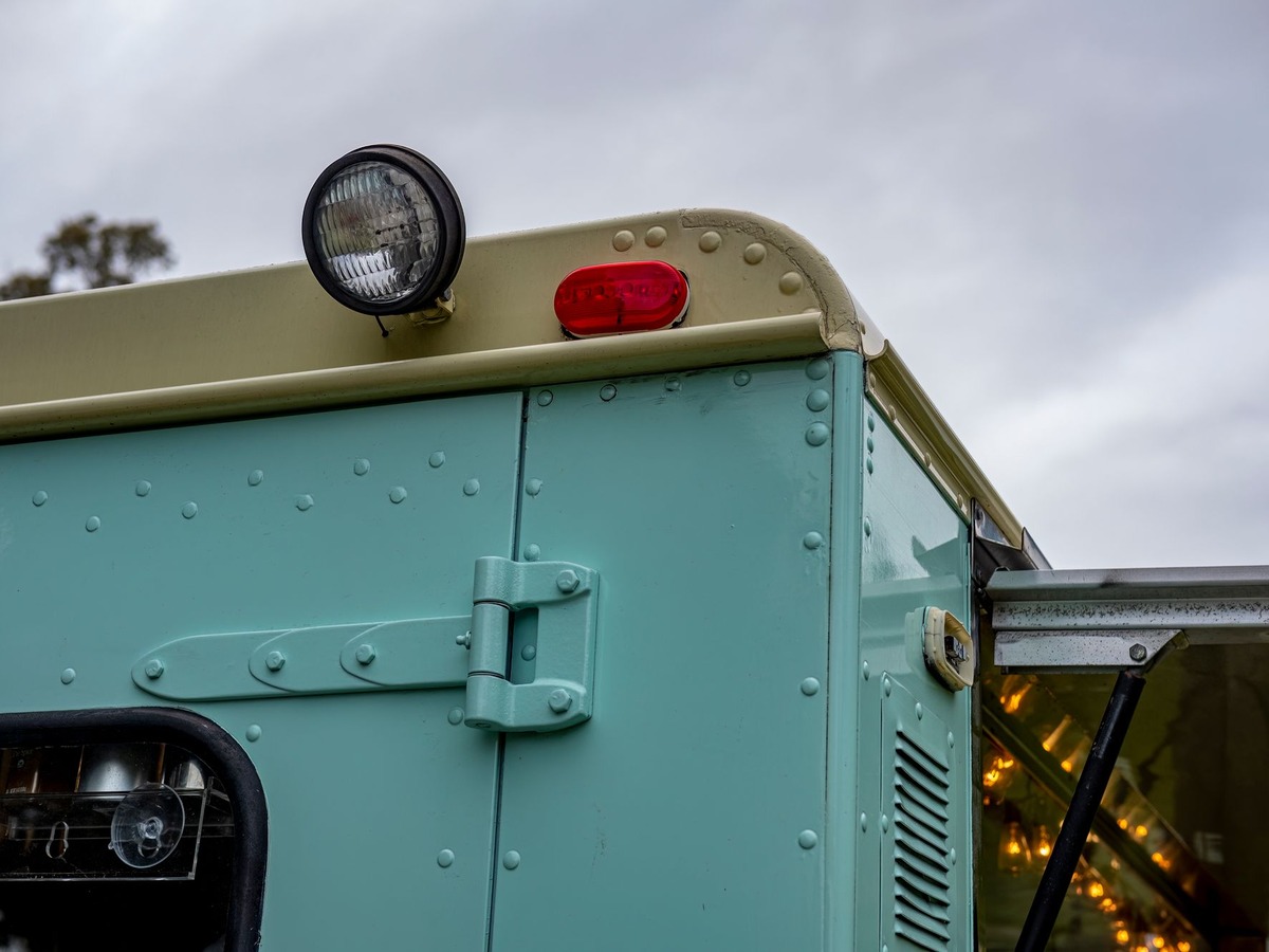 Détail de la façade d'un food truck ancien vert d'eau, avec son phare, son feu rouge et son comptoir de service