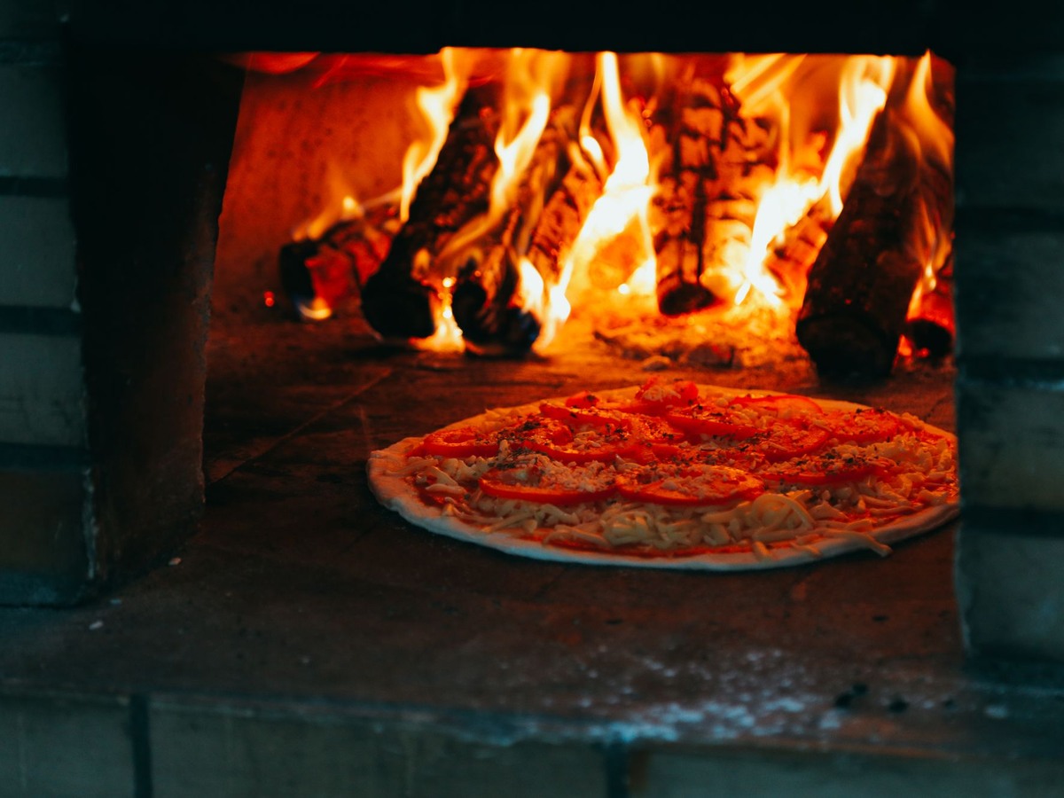 Pizza en cuisson dans un four à bois, devant les flammes