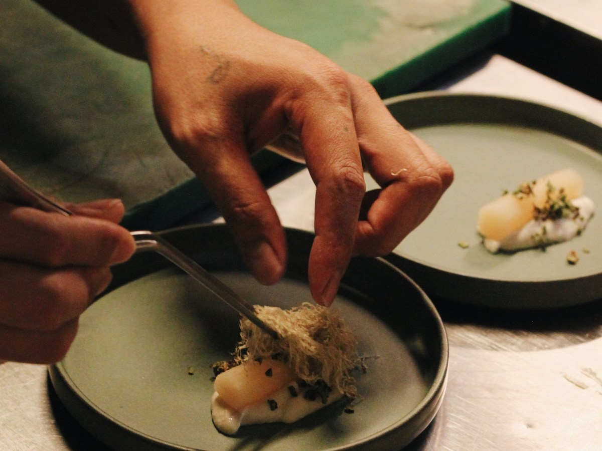 Mains d'un cuisinier dressant une assiette gastronomique avec une crème et des herbes