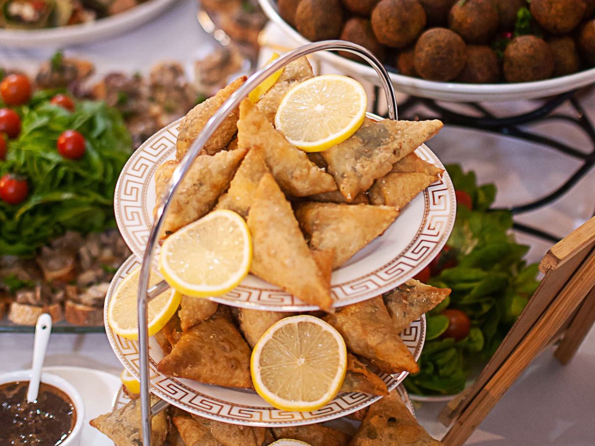 Buffet de traiteur : samosas et rondelles de citron sur un présentoir à étages, salade et boulettes à l'arrière-plan